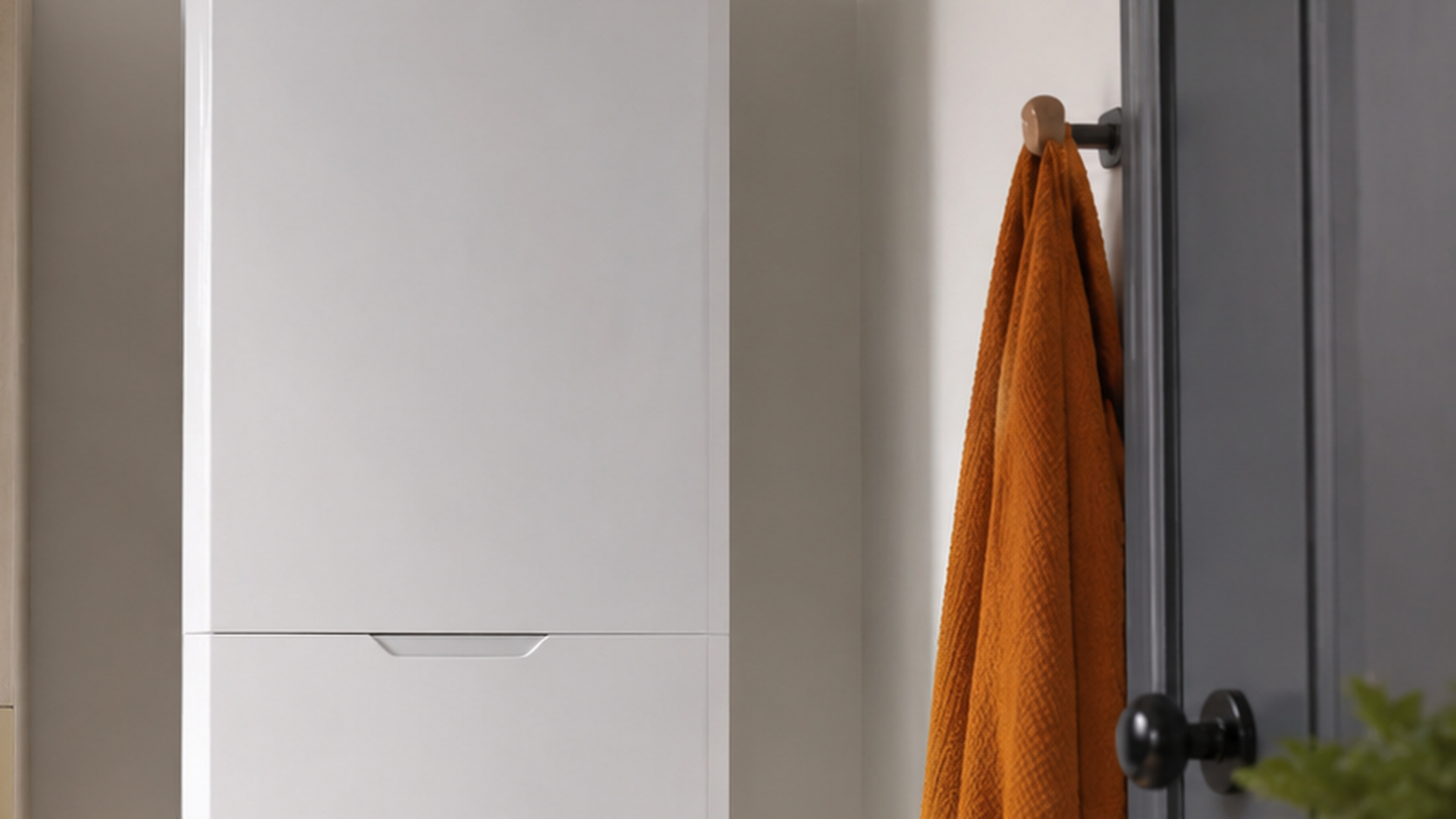 Modern white wall-mounted boiler in a tidy UK utility room with an orange towel on the wall