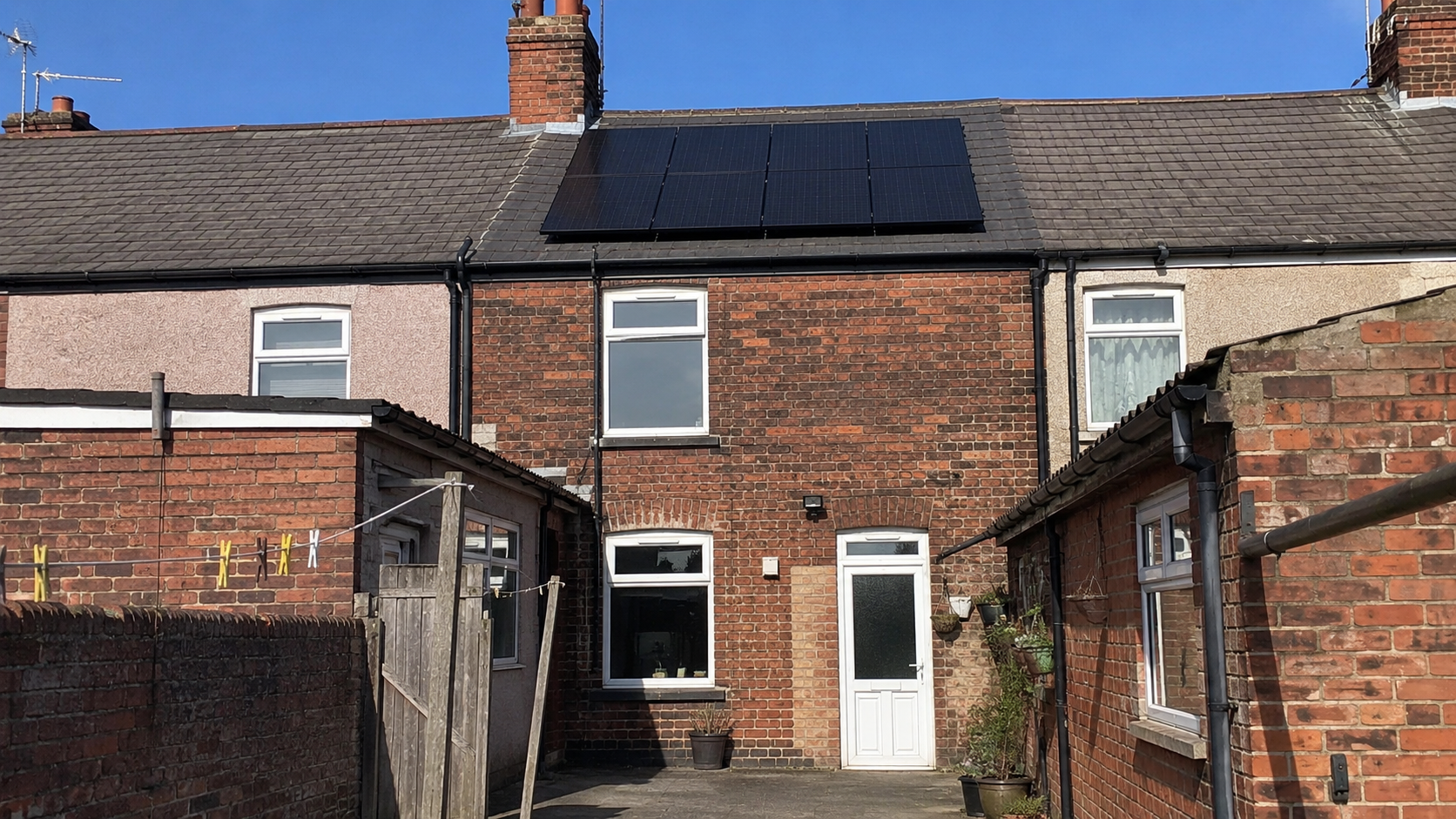Red-brick UK terrace rear yard with dark solar panels on the back roof pitch, washing line and alley gate
